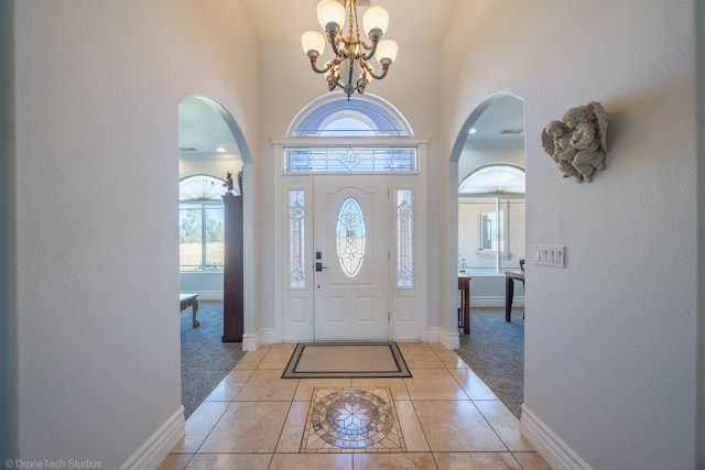 entryway with a notable chandelier, a towering ceiling, and light tile patterned floors