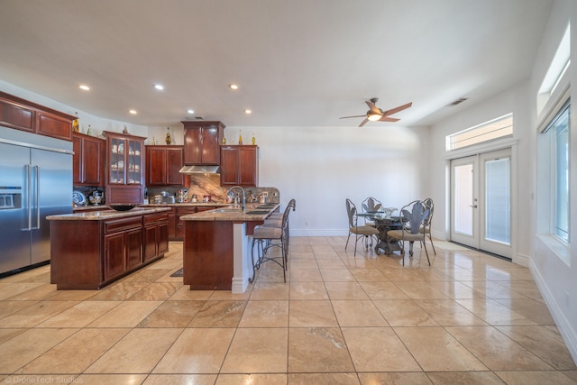 kitchen with stainless steel built in refrigerator, backsplash, light stone countertops, ceiling fan, and french doors