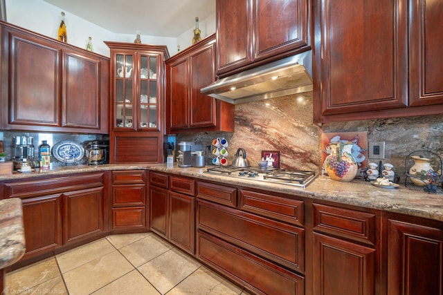 kitchen with stainless steel gas stovetop, backsplash, light stone countertops, and light tile patterned floors