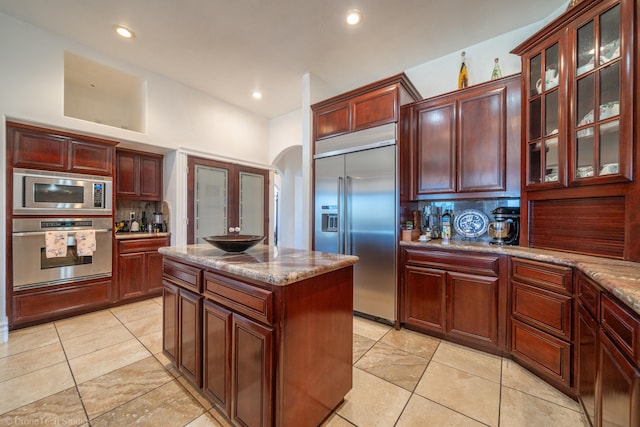 kitchen with decorative backsplash, a center island, built in appliances, and light stone countertops