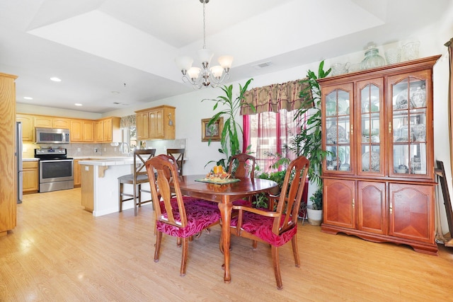 dining space featuring light hardwood / wood-style floors, a tray ceiling, and an inviting chandelier