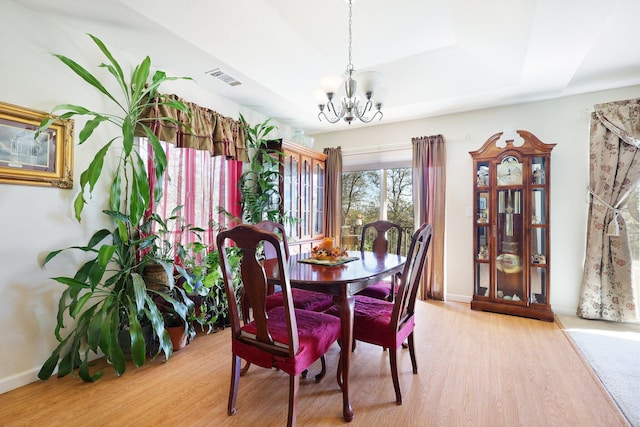 dining area featuring light hardwood / wood-style floors, a tray ceiling, and a notable chandelier