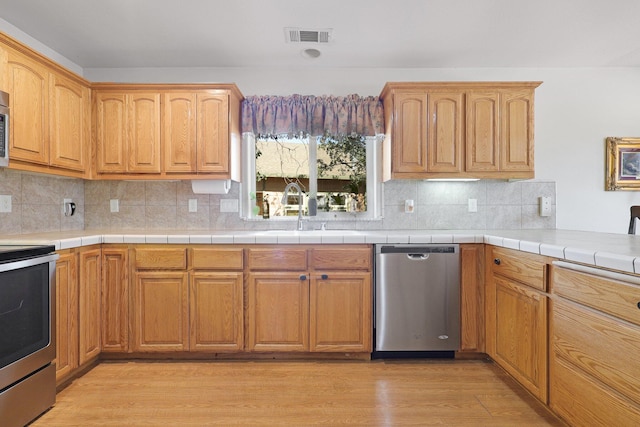 kitchen with sink, tasteful backsplash, light hardwood / wood-style flooring, stainless steel appliances, and tile countertops