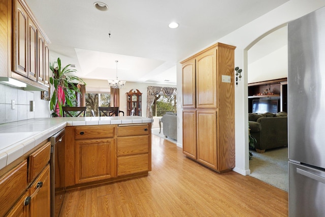 kitchen with kitchen peninsula, a chandelier, stainless steel appliances, tile counters, and light hardwood / wood-style floors