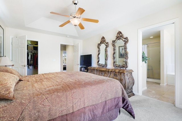 carpeted bedroom featuring a tray ceiling, a closet, connected bathroom, a walk in closet, and ceiling fan