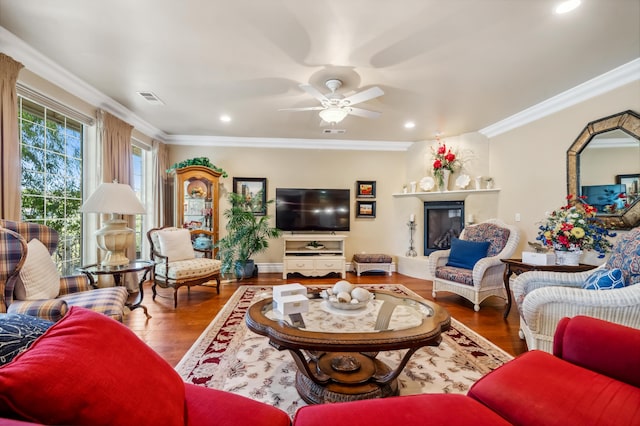 living room with a large fireplace, ornamental molding, hardwood / wood-style flooring, and ceiling fan