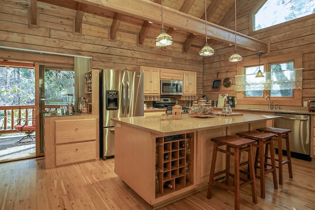 kitchen with appliances with stainless steel finishes, light stone counters, wood walls, a center island, and decorative light fixtures