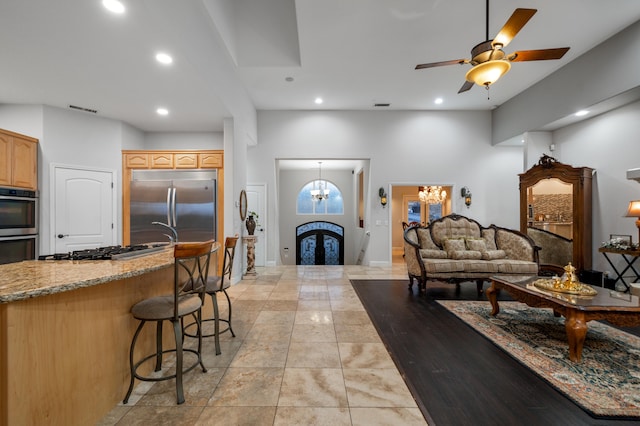 kitchen featuring a breakfast bar area, appliances with stainless steel finishes, light tile patterned flooring, ceiling fan with notable chandelier, and light stone counters