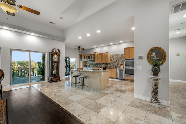 kitchen featuring tasteful backsplash, appliances with stainless steel finishes, a kitchen island, light stone counters, and a breakfast bar area