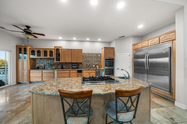 kitchen with a large island with sink, sink, a kitchen bar, stainless steel appliances, and decorative backsplash