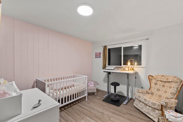 bedroom featuring light hardwood / wood-style floors, wooden walls, and a nursery area