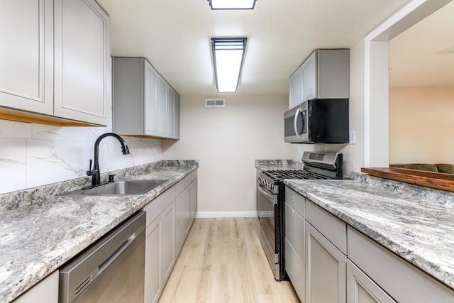 kitchen with light stone counters, stainless steel appliances, sink, light hardwood / wood-style flooring, and gray cabinets