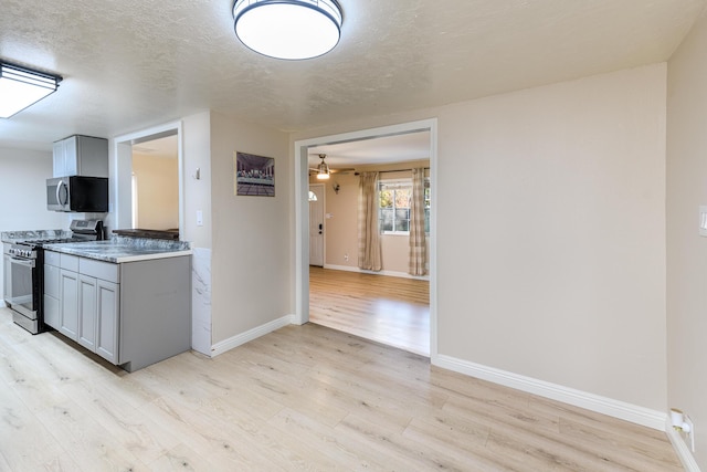 kitchen with gray cabinets, a textured ceiling, appliances with stainless steel finishes, light hardwood / wood-style floors, and light stone counters