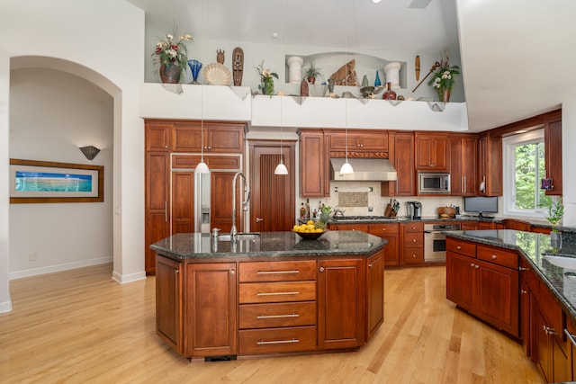 kitchen with range hood, an island with sink, decorative light fixtures, and light hardwood / wood-style floors