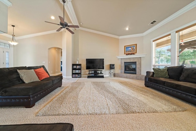 carpeted living room featuring ceiling fan, crown molding, and a tiled fireplace