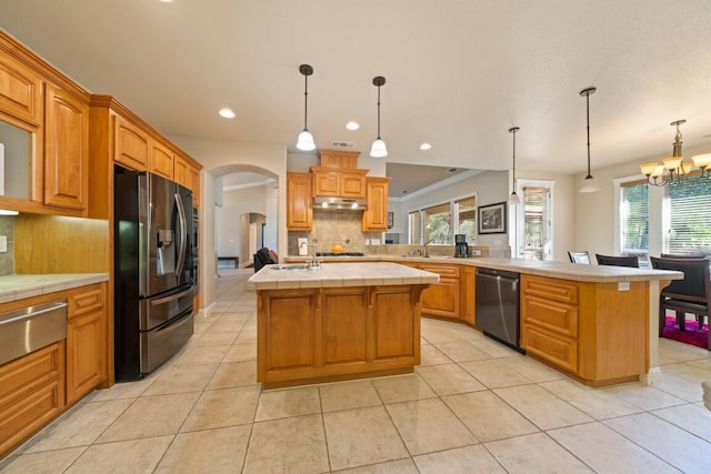 kitchen with an island with sink, hanging light fixtures, stainless steel appliances, and tasteful backsplash