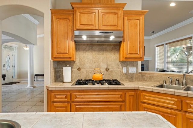 kitchen featuring decorative columns, tile counters, stainless steel gas stovetop, and sink