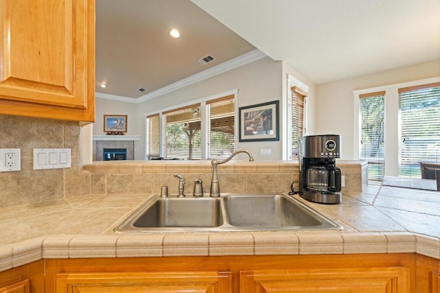 kitchen with a tile fireplace, tasteful backsplash, sink, tile counters, and kitchen peninsula