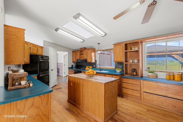 kitchen with a skylight, light wood-type flooring, tasteful backsplash, black double oven, and a center island