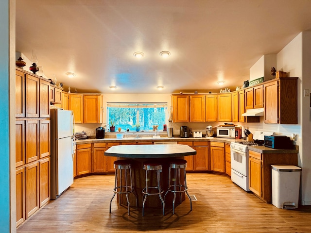 kitchen with white appliances, a center island, light hardwood / wood-style floors, and a breakfast bar area