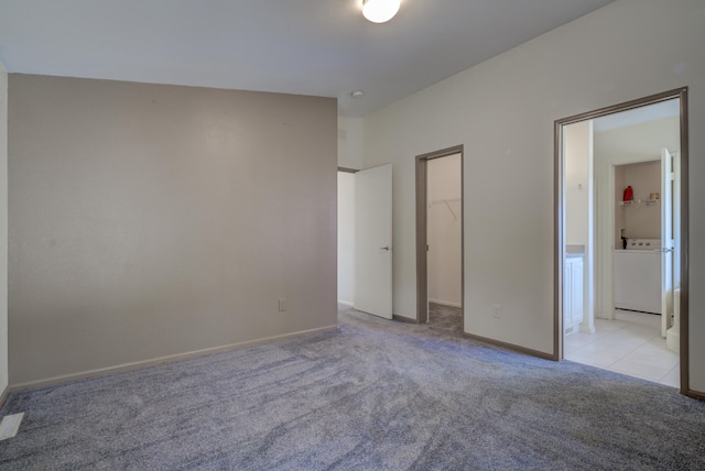 unfurnished bedroom with a walk in closet, washer / clothes dryer, a closet, light colored carpet, and ensuite bathroom