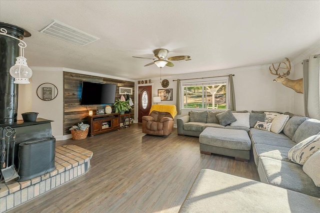 living room with wood walls, wood-type flooring, crown molding, and ceiling fan