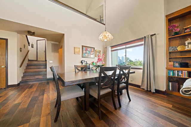 dining area with a towering ceiling, a chandelier, and dark wood-type flooring