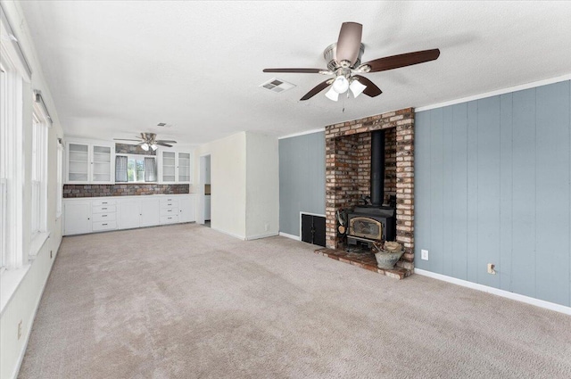 unfurnished living room featuring light colored carpet, a wood stove, ceiling fan, and wood walls