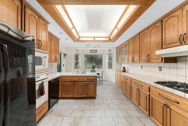 kitchen featuring decorative backsplash, a raised ceiling, sink, tile countertops, and black appliances