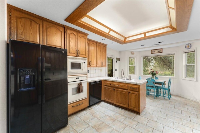 kitchen with black appliances, sink, kitchen peninsula, a tray ceiling, and tile countertops