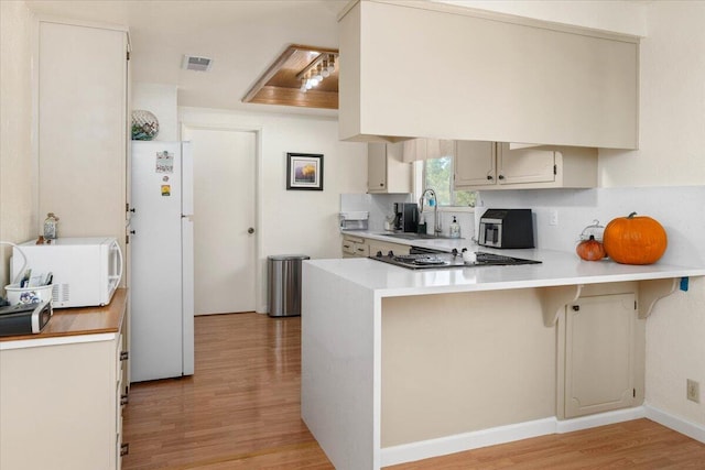 kitchen with kitchen peninsula, white appliances, sink, and light hardwood / wood-style floors