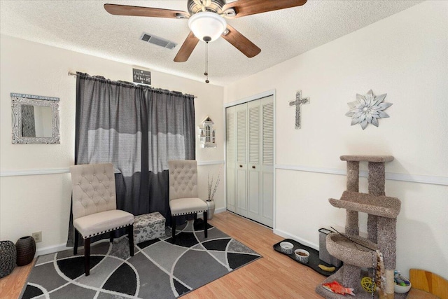 living area with ceiling fan, hardwood / wood-style floors, and a textured ceiling