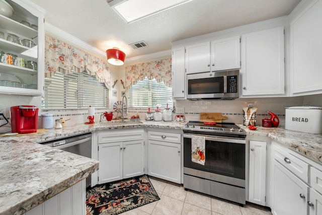 kitchen with sink, white cabinets, light tile patterned floors, light stone counters, and stainless steel appliances