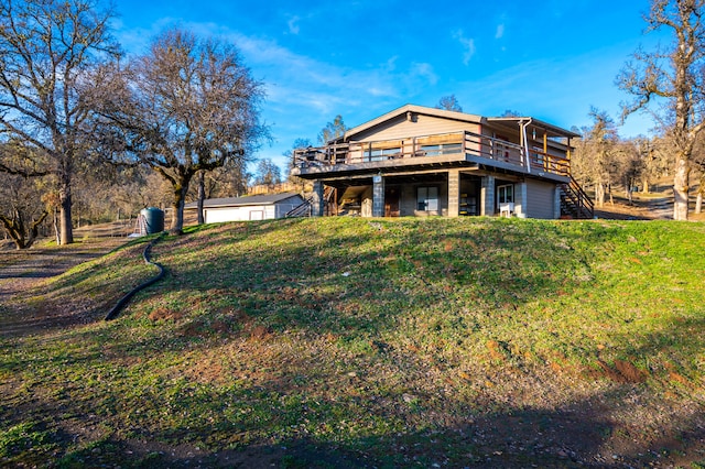 back of house featuring a garage, an outbuilding, a lawn, and a wooden deck