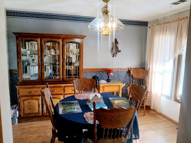 dining space featuring light hardwood / wood-style flooring, a chandelier, and a textured ceiling