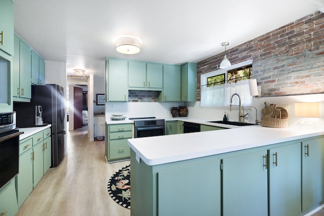 kitchen with black appliances, sink, kitchen peninsula, light hardwood / wood-style floors, and brick wall