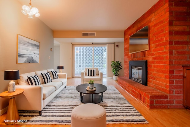 living room with a brick fireplace, light hardwood / wood-style flooring, and an inviting chandelier