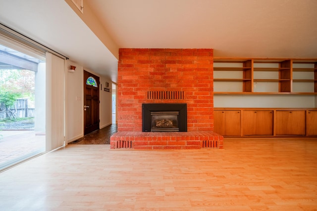 unfurnished living room with light wood-type flooring and a brick fireplace