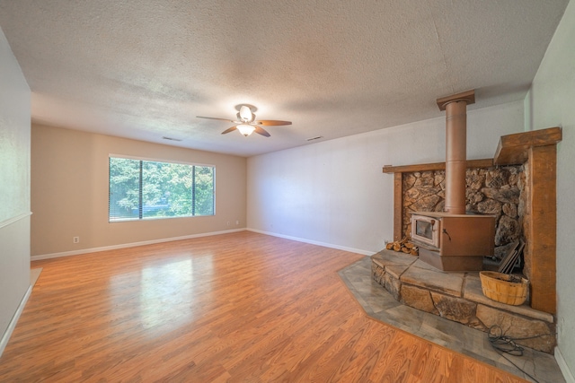 unfurnished living room featuring a textured ceiling, hardwood / wood-style flooring, a wood stove, and ceiling fan