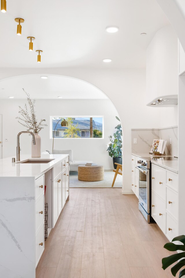 kitchen featuring sink, light stone counters, stainless steel range, an island with sink, and white cabinets