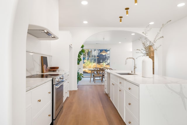 kitchen with sink, light stone counters, stainless steel range with electric stovetop, light wood-type flooring, and white cabinets