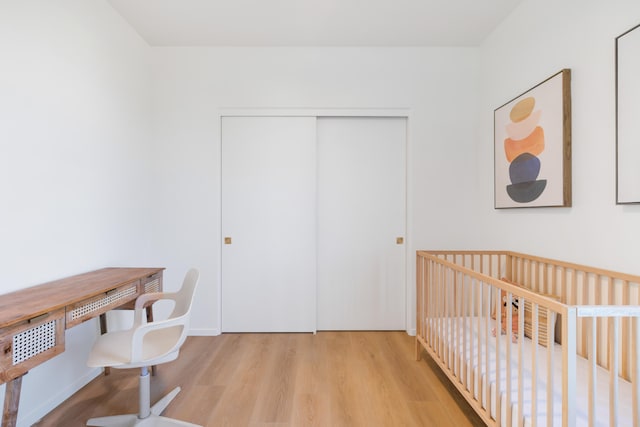 bedroom with a crib, a closet, and light wood-type flooring