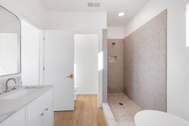 bathroom with hardwood / wood-style flooring, vanity, a tile shower, and toilet