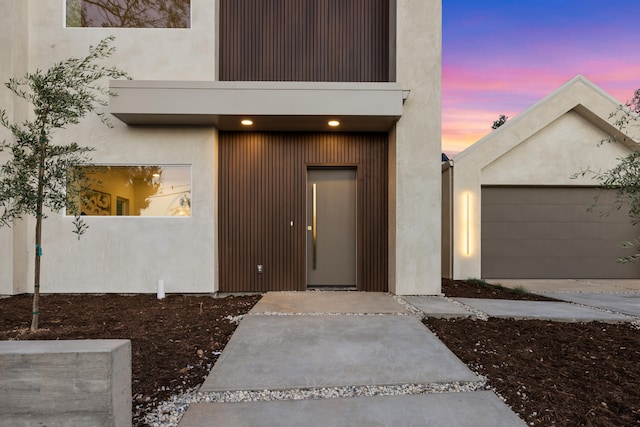 exterior entry at dusk with a garage and a balcony