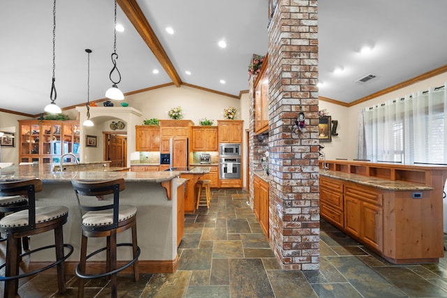 kitchen featuring a large island with sink, stainless steel appliances, decorative columns, a kitchen bar, and decorative light fixtures