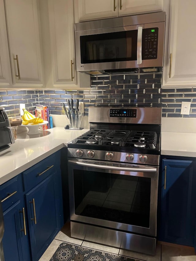 kitchen featuring white cabinets, blue cabinetry, decorative backsplash, and appliances with stainless steel finishes