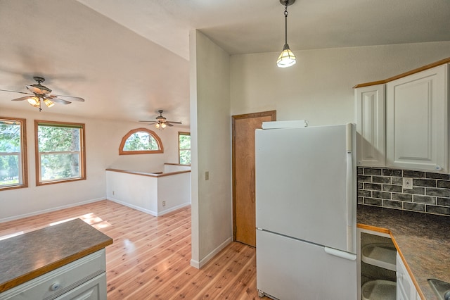 kitchen featuring lofted ceiling, tasteful backsplash, light wood-type flooring, decorative light fixtures, and white refrigerator