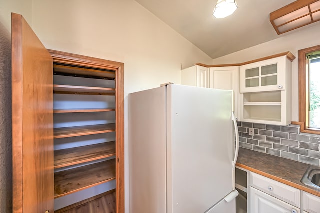 kitchen featuring decorative backsplash, white cabinets, wood-type flooring, vaulted ceiling, and white refrigerator