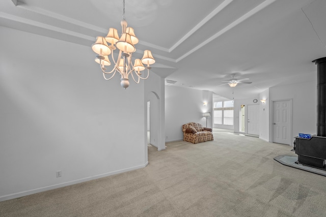 unfurnished living room featuring a wood stove, light carpet, and ceiling fan with notable chandelier