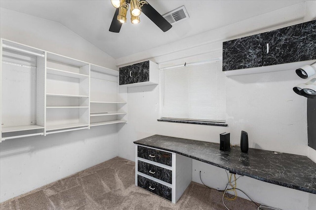 spacious closet with carpet flooring, built in desk, vaulted ceiling, and ceiling fan